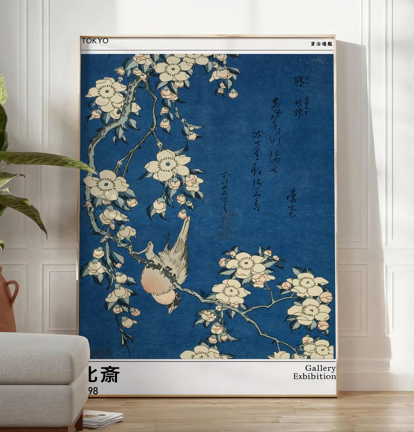 Reproduction affiche Hokusai bouvreuil et cerisier, posee au sol dans un salon minimaliste clair, a cote d'un canape beige et d'une plante verte, sur un parquet clair
