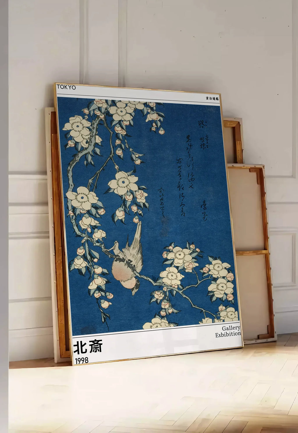 Tirage encadrable affiche Hokusai bouvreuil et cerisier, posee au sol dans une entree lumineuse, contre un mur a panneaux blancs, a cote de chassis en bois empiles