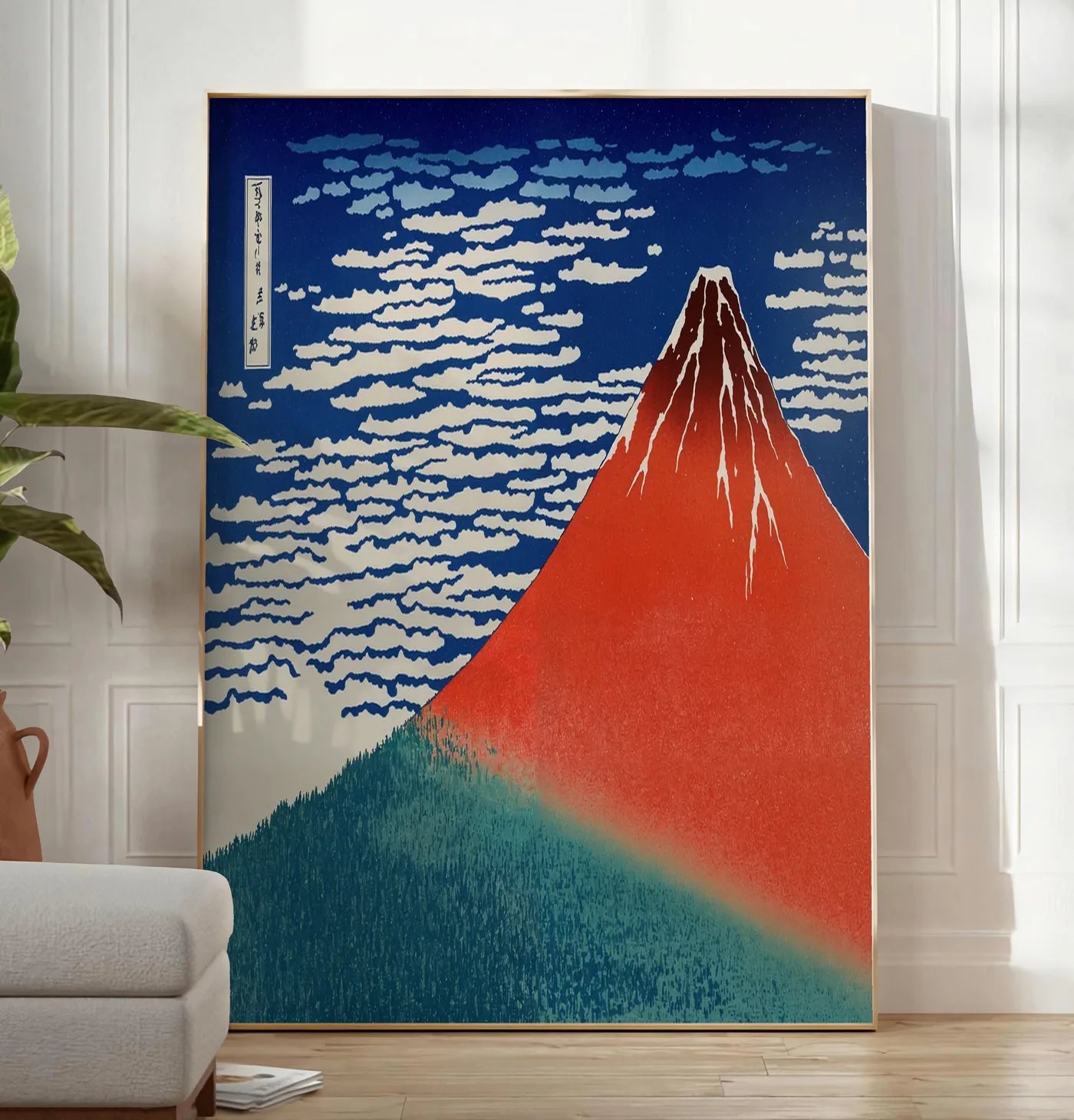 Reproduction affiche mont Fuji rouge de Hokusai art japonais, posee au sol dans un salon minimaliste clair, a cote d'un canape beige et d'une plante verte, sur un parquet clair