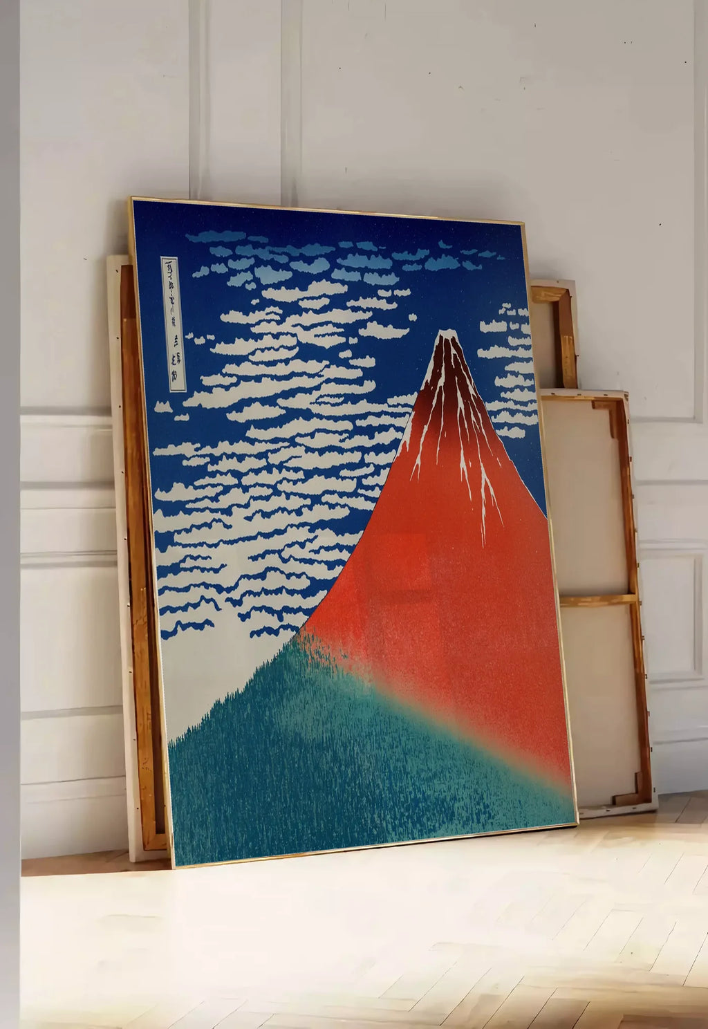 Tirage encadrable affiche mont Fuji rouge de Hokusai art japonais, posee au sol dans une entree lumineuse, contre un mur a panneaux blancs, a cote de chassis en bois empiles