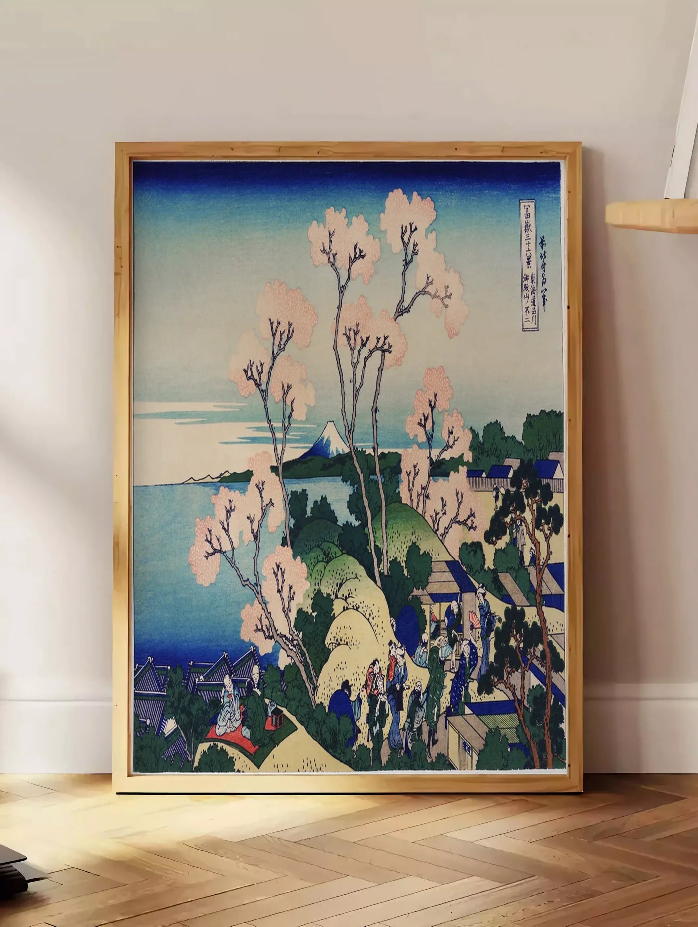 Estampe affiche cerisiers de Goten-yama de Hokusai art japonais, posee au sol dans un coin salon, sur un parquet a chevrons, pres d'une table d'appoint en chene chargee de livres