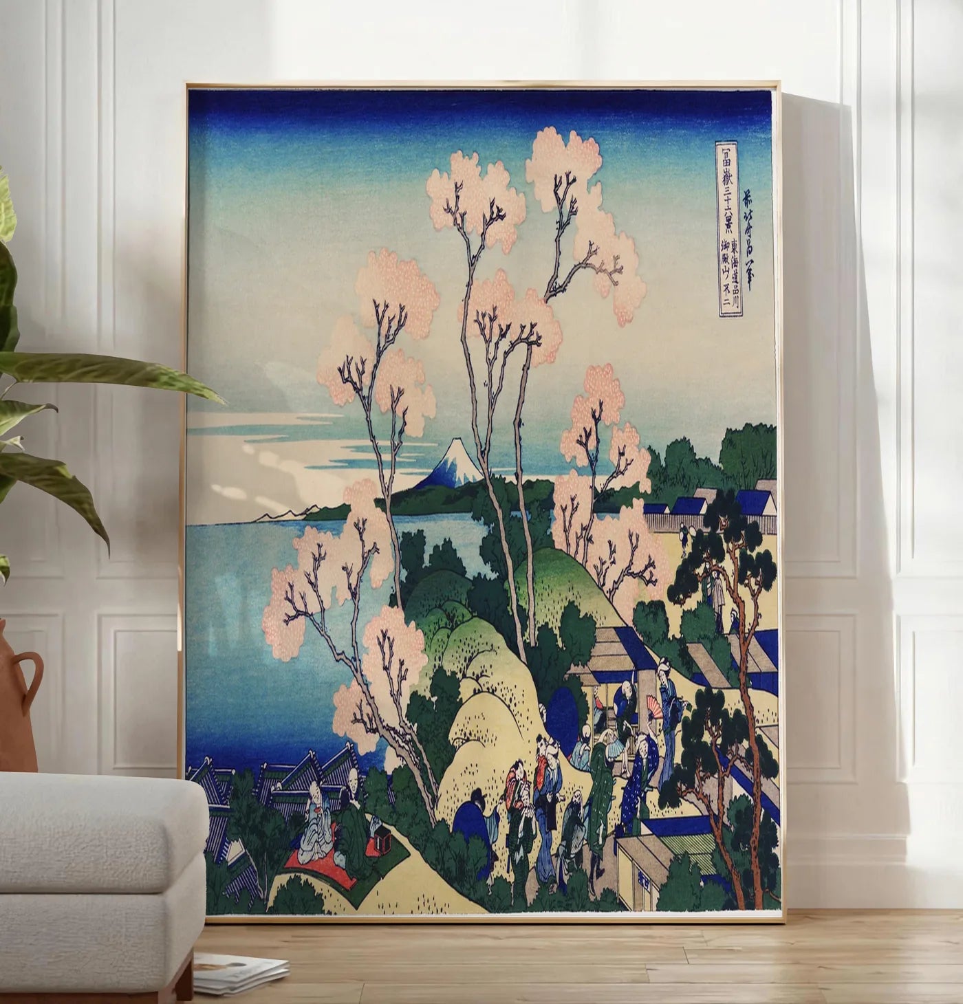Reproduction affiche cerisiers de Goten-yama de Hokusai art japonais, posee au sol dans un salon minimaliste clair, a cote d'un canape beige et d'une plante verte, sur un parquet clair