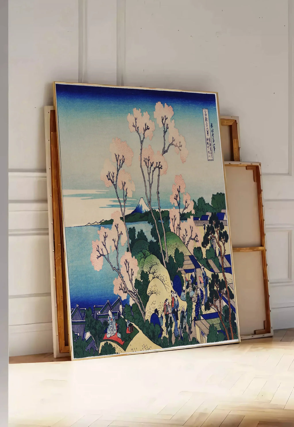 Tirage encadrable affiche cerisiers de Goten-yama de Hokusai art japonais, posee au sol dans une entree lumineuse, contre un mur a panneaux blancs, a cote de chassis en bois empiles