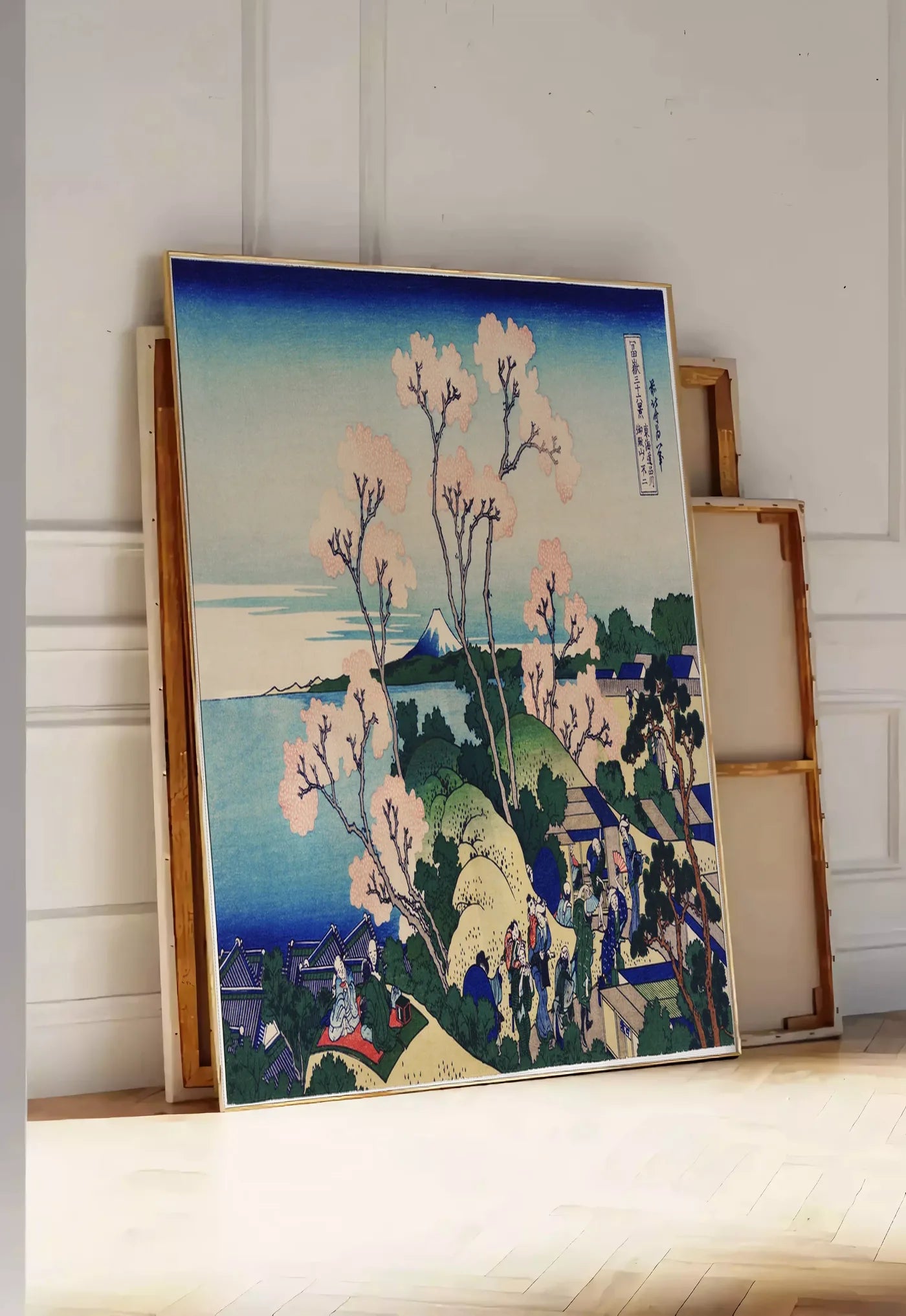 Tirage encadrable affiche cerisiers de Goten-yama de Hokusai art japonais, posee au sol dans une entree lumineuse, contre un mur a panneaux blancs, a cote de chassis en bois empiles