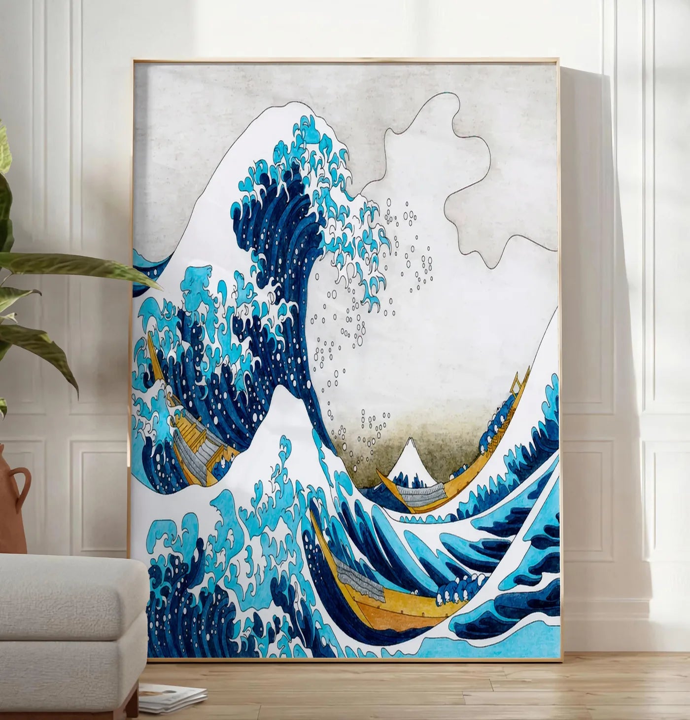 Reproduction affiche Hokusai grande vague coloree, posee au sol dans un salon minimaliste clair, a cote d'un canape beige et d'une plante verte, sur un parquet clair