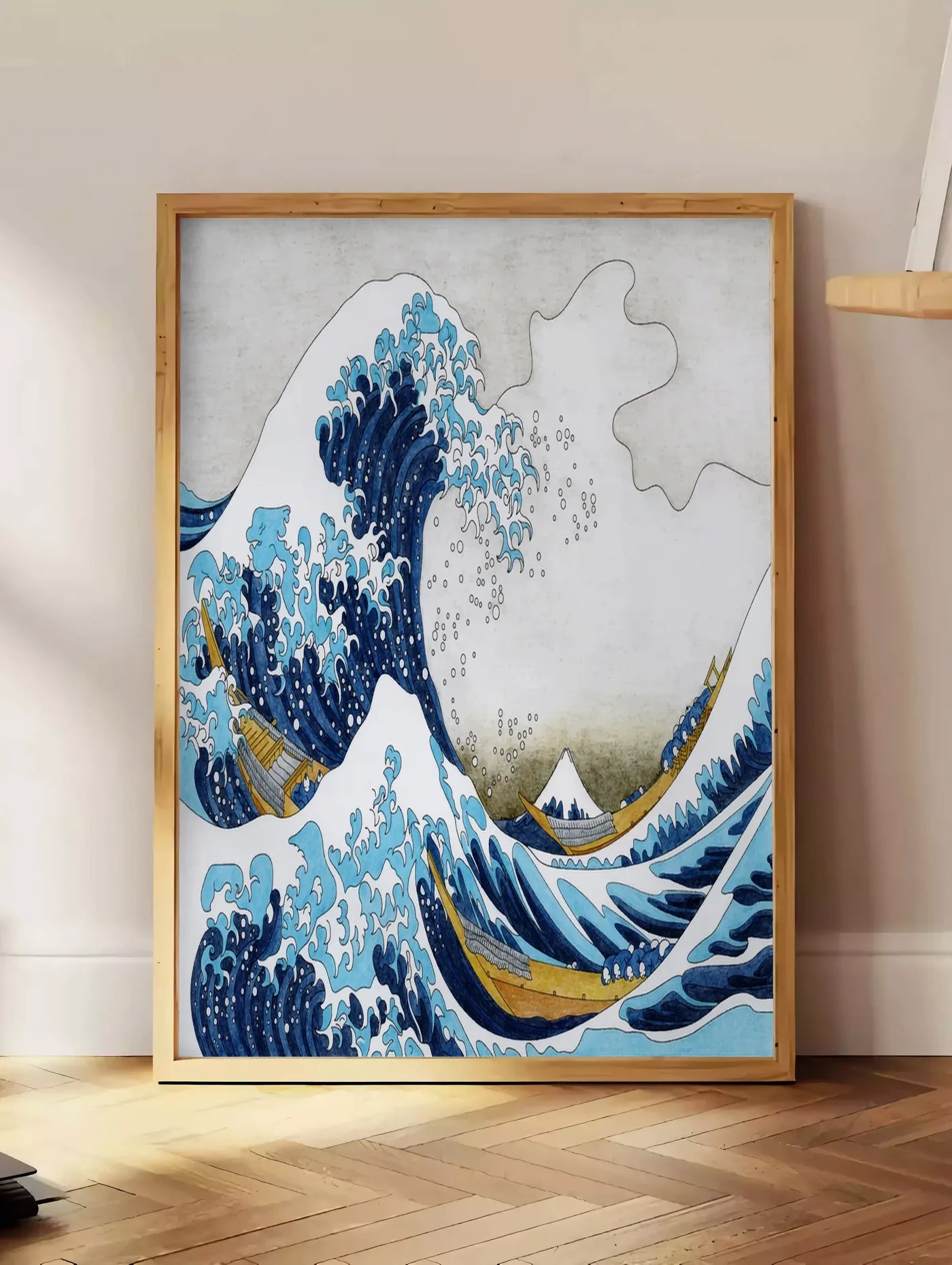 Estampe affiche Hokusai grande vague et barques de pecheurs, posee au sol dans un coin salon, sur un parquet a chevrons, pres d'une table d'appoint en chene chargee de livres