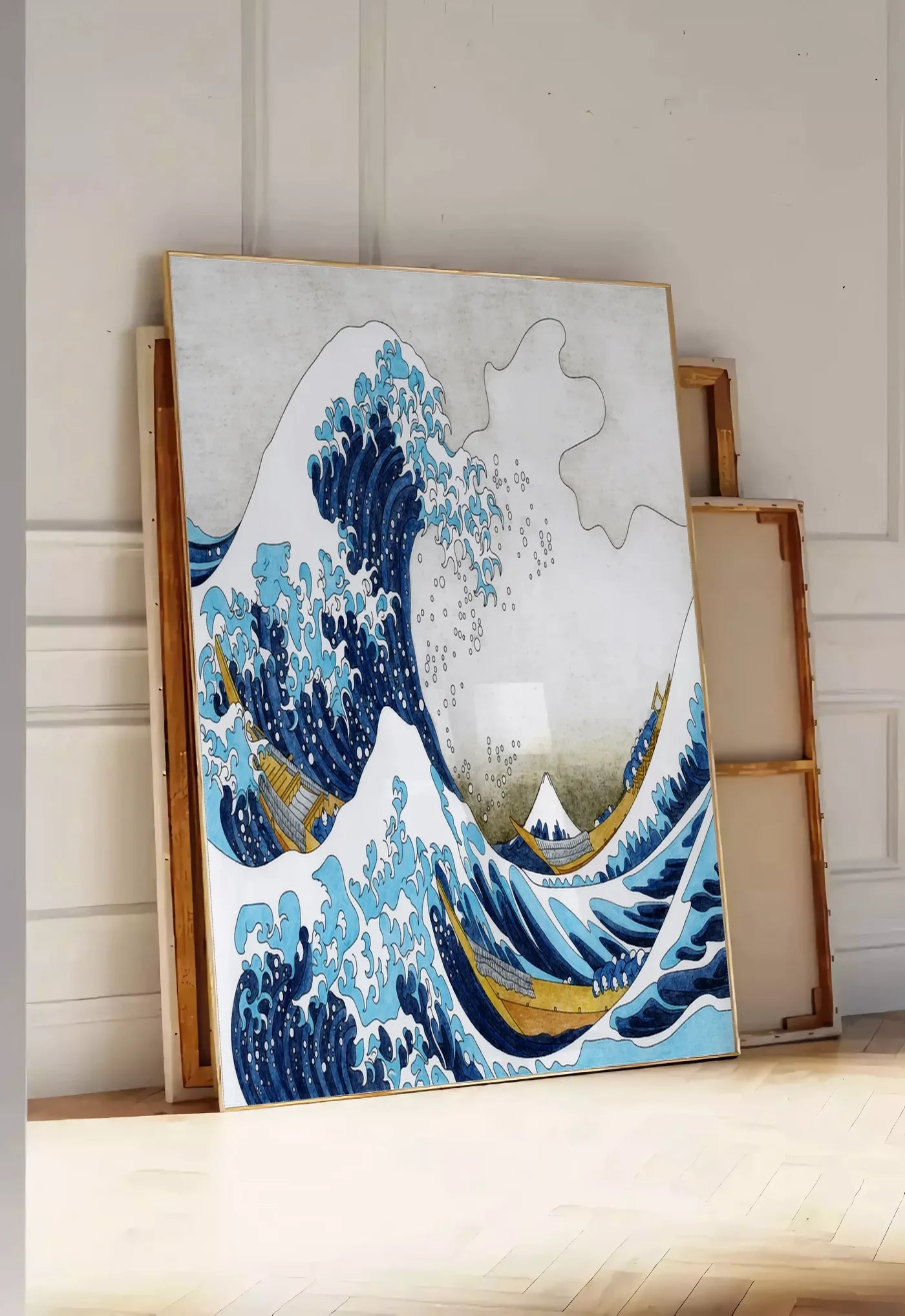Tirage encadrable affiche Hokusai grande vague et barques de pecheurs, posee au sol dans une entree lumineuse, contre un mur a panneaux blancs, a cote de chassis en bois empiles