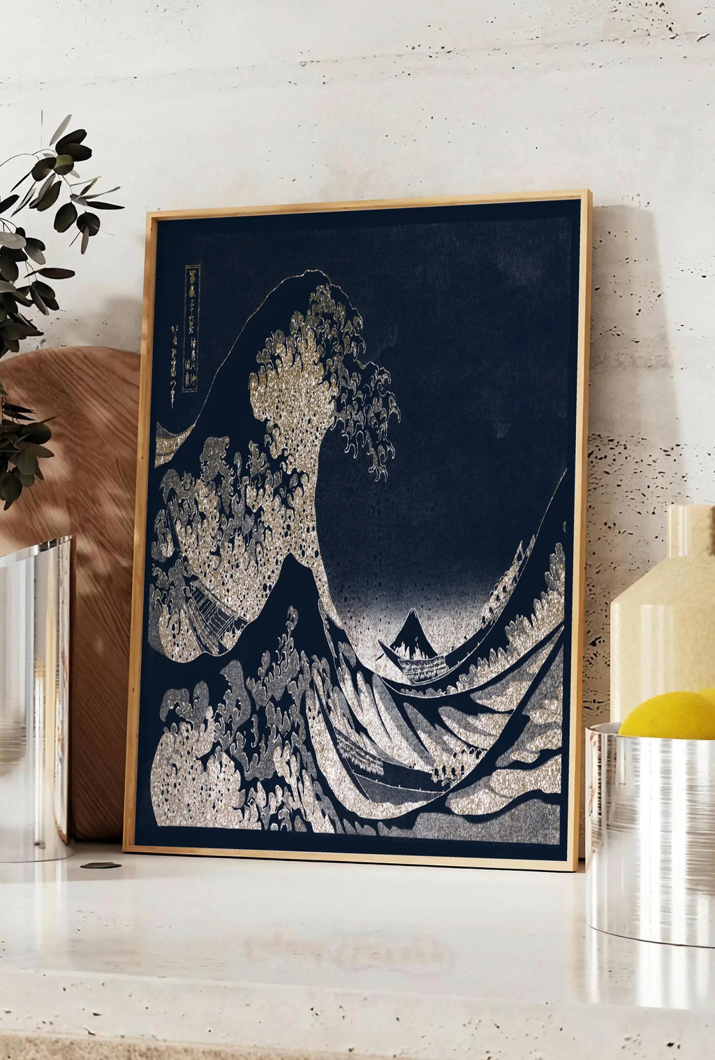 Affiche affiche Hokusai grande vague doree sur bleu nuit, posee sur un plan de travail de cuisine en pierre claire, entre une branche d'eucalyptus en vase et un bocal de citrons