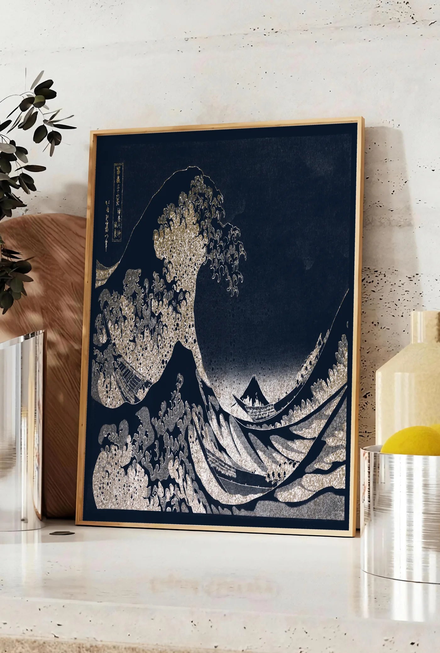 Affiche affiche Hokusai grande vague doree sur bleu nuit, posee sur un plan de travail de cuisine en pierre claire, entre une branche d'eucalyptus en vase et un bocal de citrons