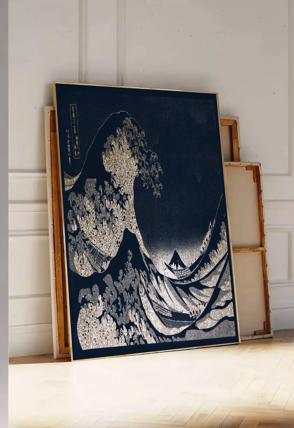 Tirage encadrable affiche Hokusai grande vague doree sur bleu nuit, posee au sol dans une entree lumineuse, contre un mur a panneaux blancs, a cote de chassis en bois empiles
