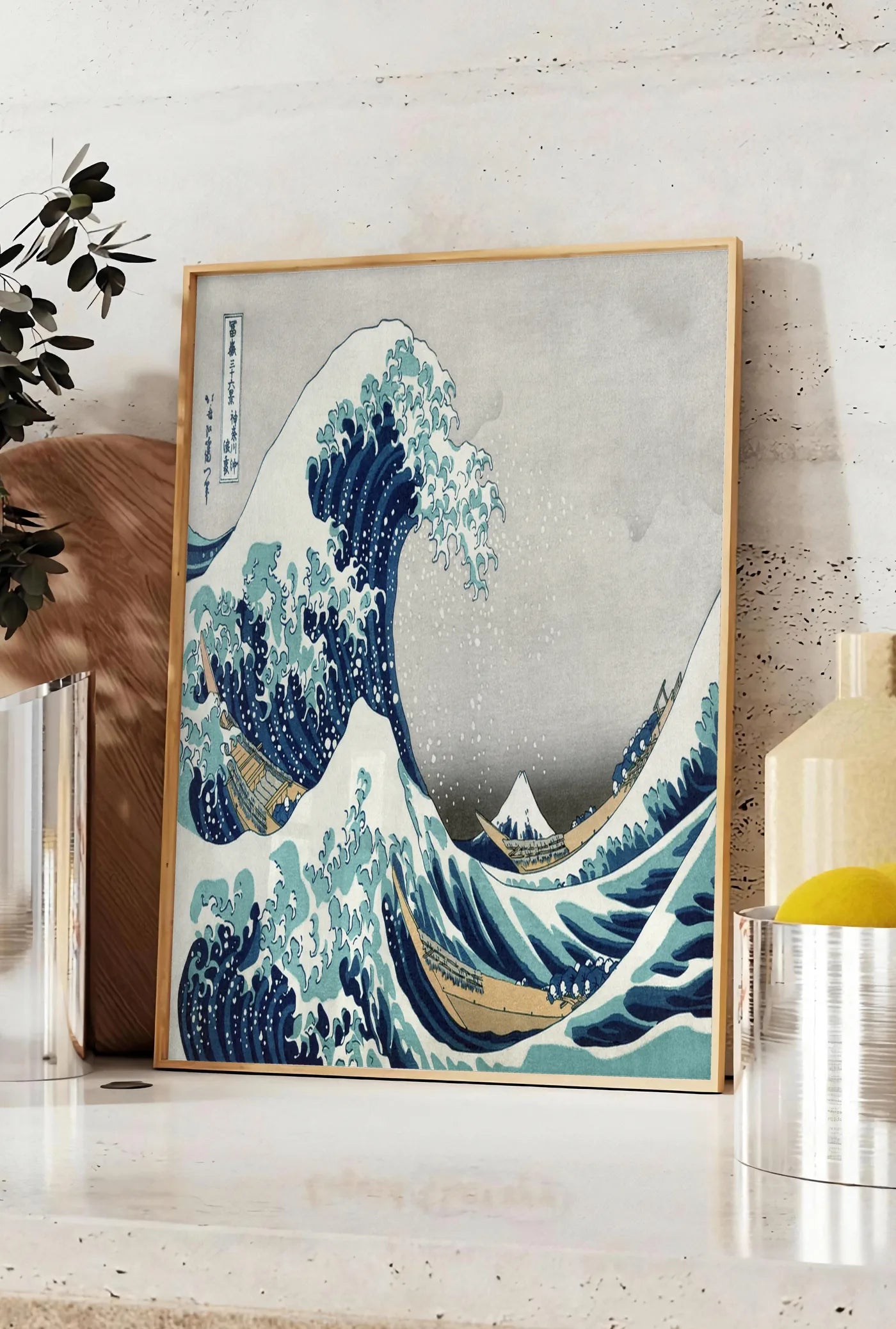 Affiche affiche grande vague de Hokusai art japonais, posee sur un plan de travail de cuisine en pierre claire, entre une branche d'eucalyptus en vase et un bocal de citrons