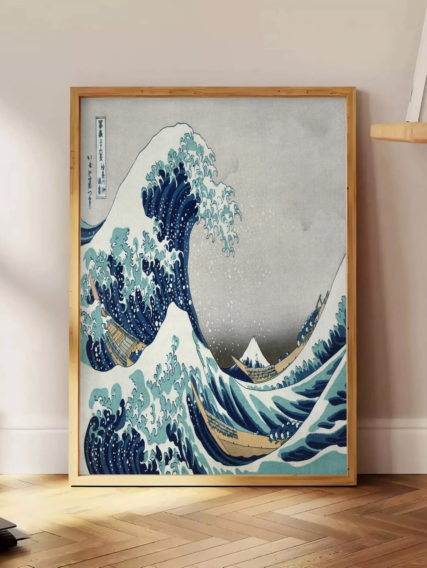 Estampe affiche grande vague de Hokusai art japonais, posee au sol dans un coin salon, sur un parquet a chevrons, pres d'une table d'appoint en chene chargee de livres