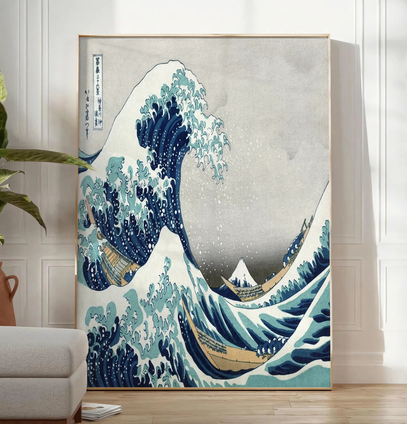 Reproduction affiche grande vague de Hokusai art japonais, posee au sol dans un salon minimaliste clair, a cote d'un canape beige et d'une plante verte, sur un parquet clair