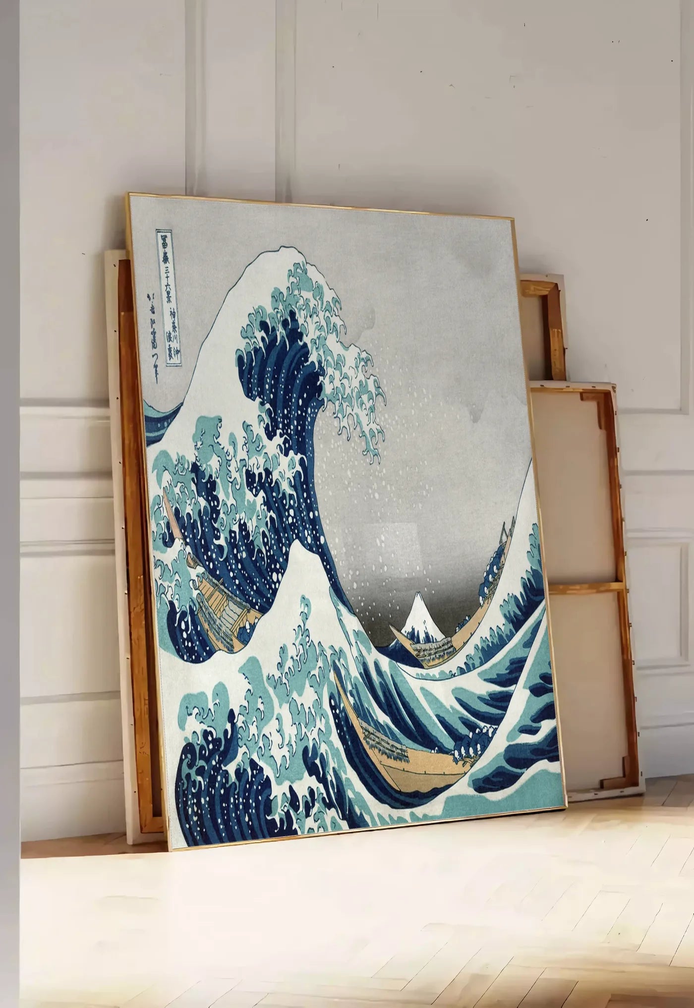 Tirage encadrable affiche grande vague de Hokusai art japonais, posee au sol dans une entree lumineuse, contre un mur a panneaux blancs, a cote de chassis en bois empiles