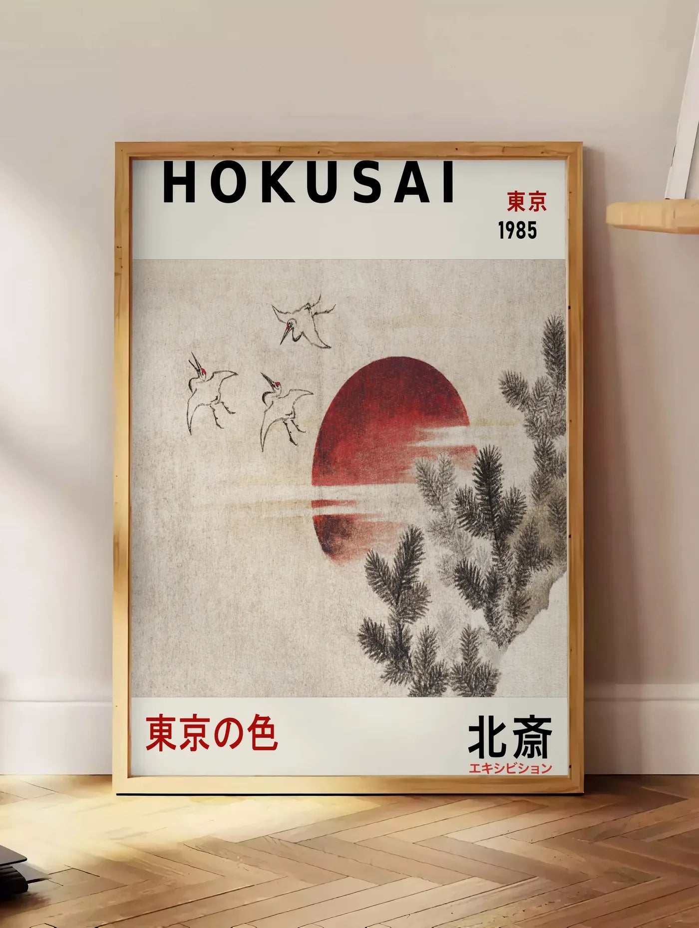 Estampe affiche Hokusai oiseaux en vol devant un soleil rouge, posee au sol dans un coin salon, sur un parquet a chevrons, pres d'une table d'appoint en chene chargee de livres
