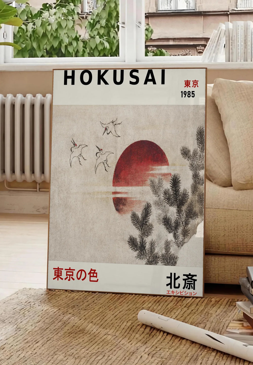 Poster affiche Hokusai oiseaux en vol devant un soleil rouge, posee au sol dans un salon parisien, devant une grande fenetre donnant sur un immeuble haussmannien, entre un ficus et un canape creme