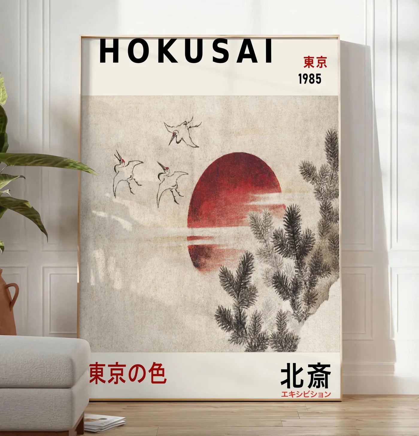 Reproduction affiche Hokusai oiseaux en vol devant un soleil rouge, posee au sol dans un salon minimaliste clair, a cote d'un canape beige et d'une plante verte, sur un parquet clair