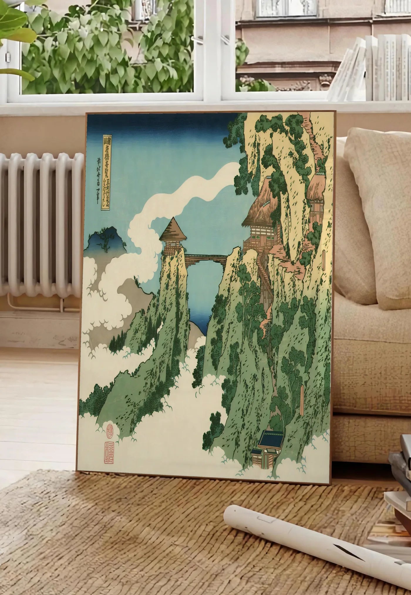 Poster affiche Hokusai pont suspendu entre falaises au-dessus des nuages, posee au sol dans un salon parisien, devant une grande fenetre donnant sur un immeuble haussmannien, entre un ficus et un canape creme