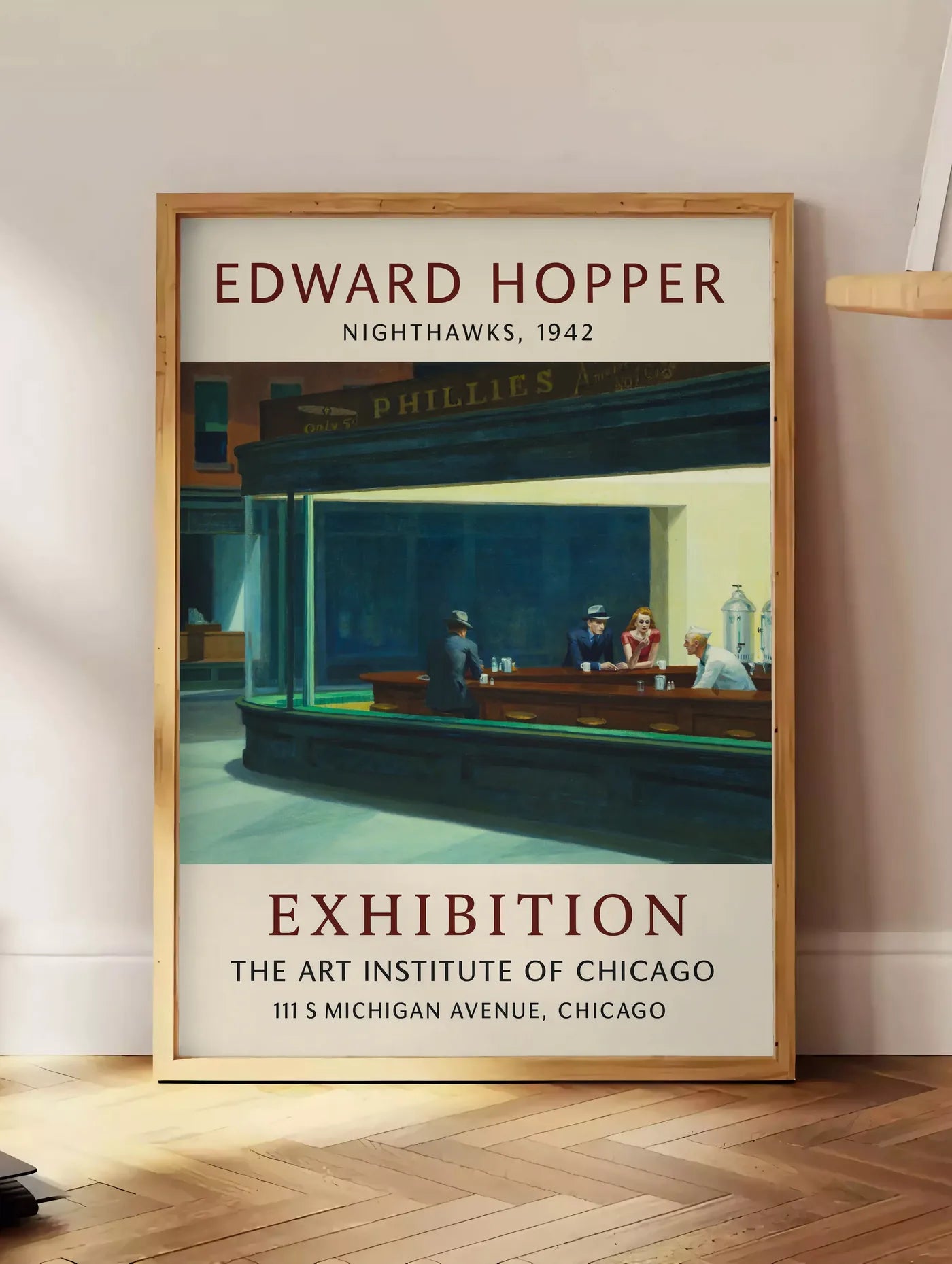 Estampe affiche Hopper Nighthawks, posee au sol dans un coin salon, sur un parquet a chevrons, pres d'une table d'appoint en chene chargee de livres