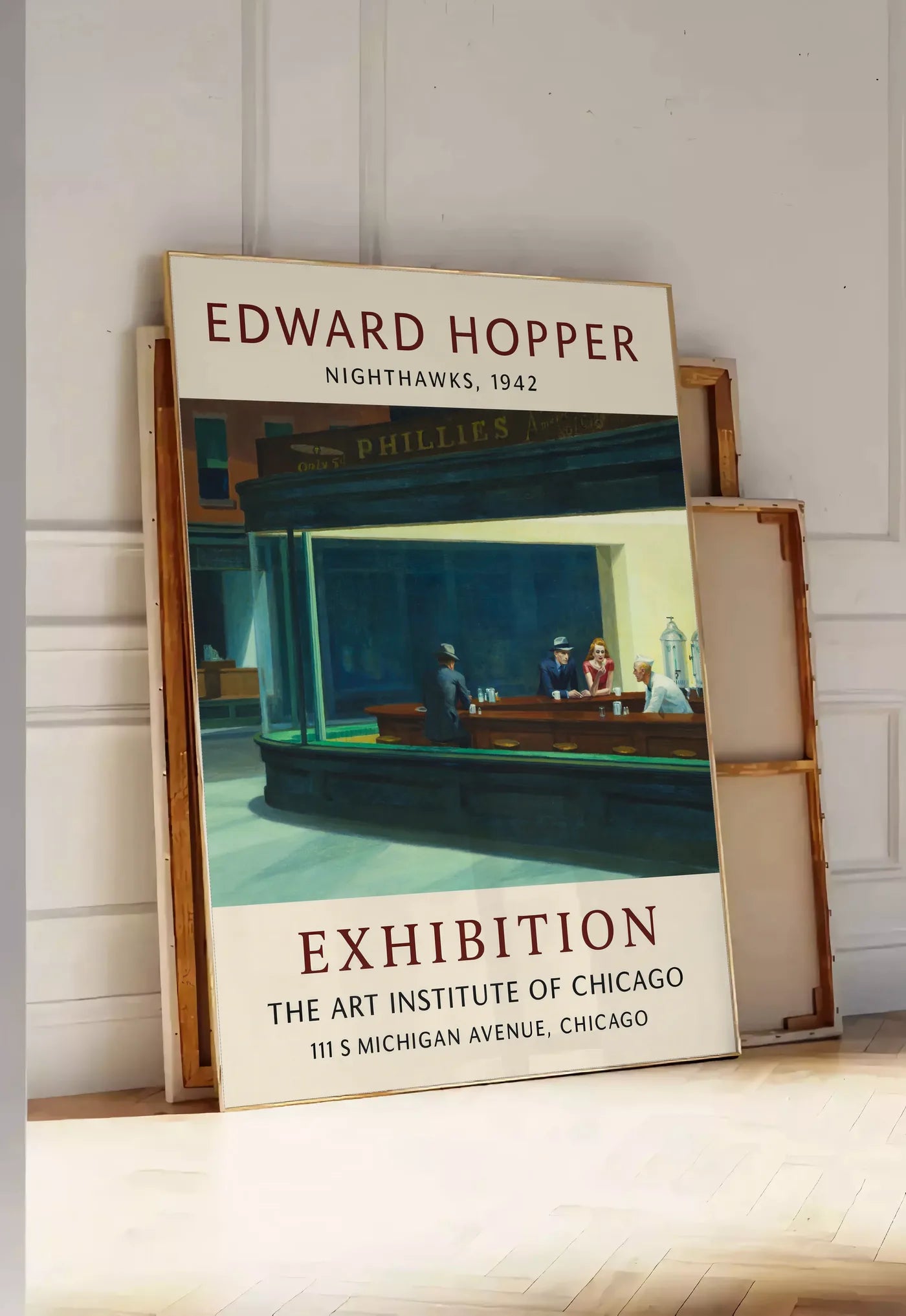 Tirage encadrable affiche Hopper Nighthawks, posee au sol dans une entree lumineuse, contre un mur a panneaux blancs, a cote de chassis en bois empiles