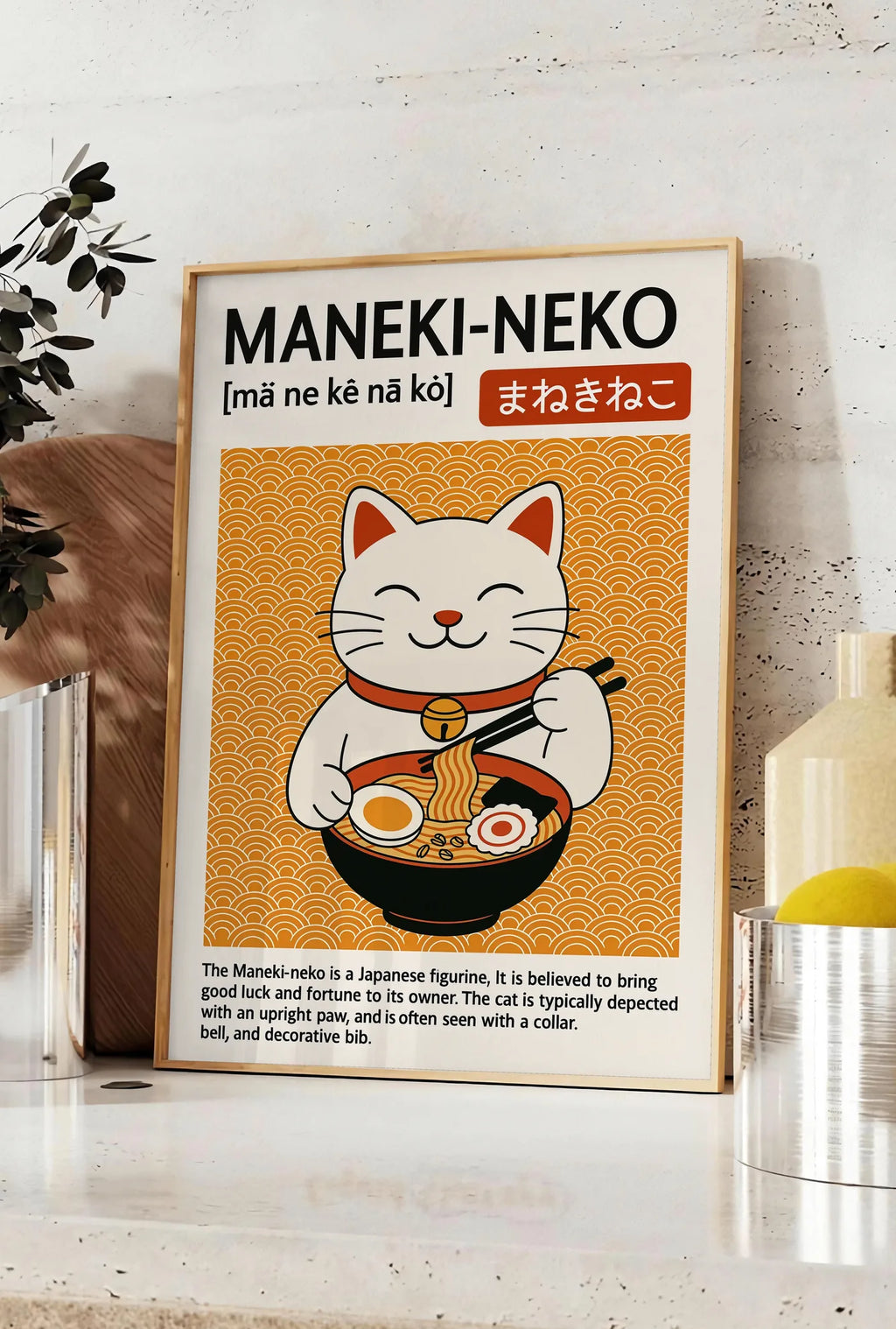 Affiche affiche Maneki-neko cuisine, posee sur un plan de travail de cuisine en pierre claire, entre une branche d'eucalyptus en vase et un bocal de citrons