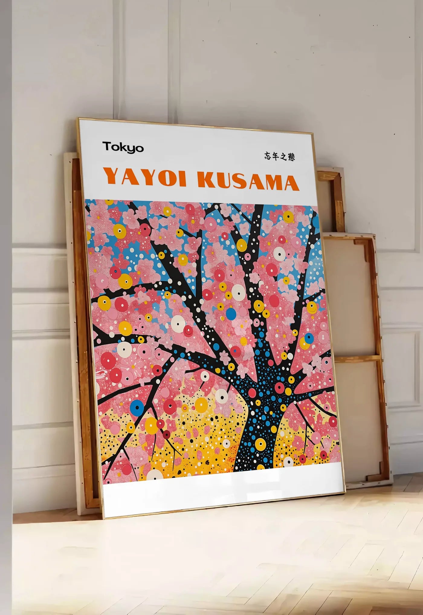 Tirage encadrable affiche cerisier a pois de Kusama art japonais, posee au sol dans une entree lumineuse, contre un mur a panneaux blancs, a cote de chassis en bois empiles