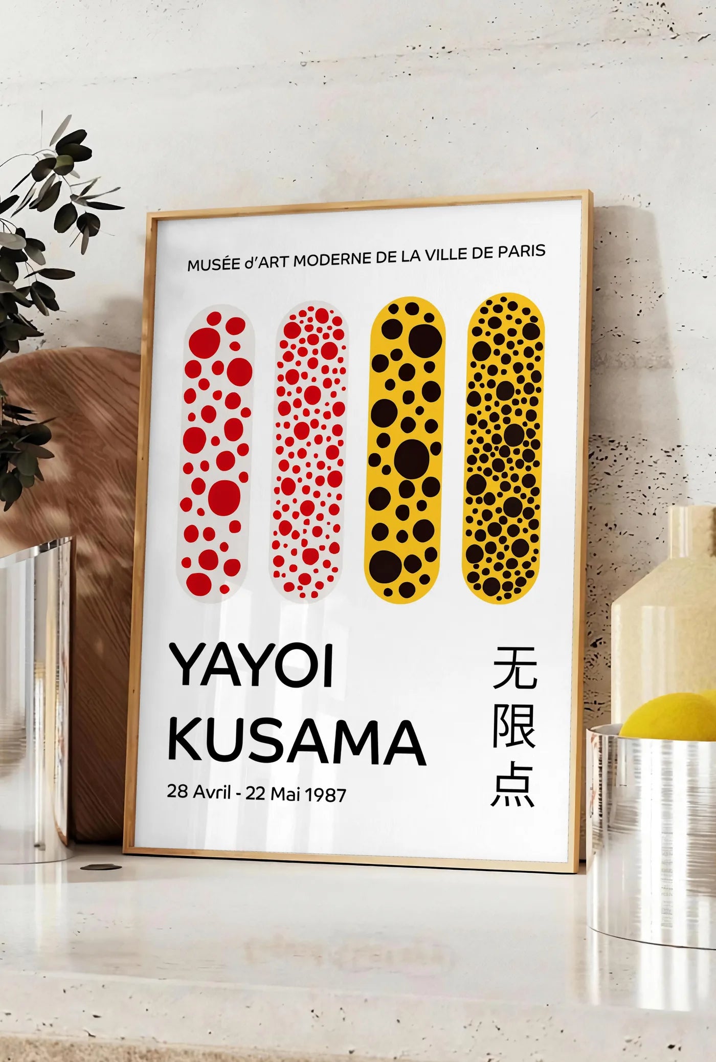 Affiche affiche capsules a pois de Kusama art japonais, posee sur un plan de travail de cuisine en pierre claire, entre une branche d'eucalyptus en vase et un bocal de citrons