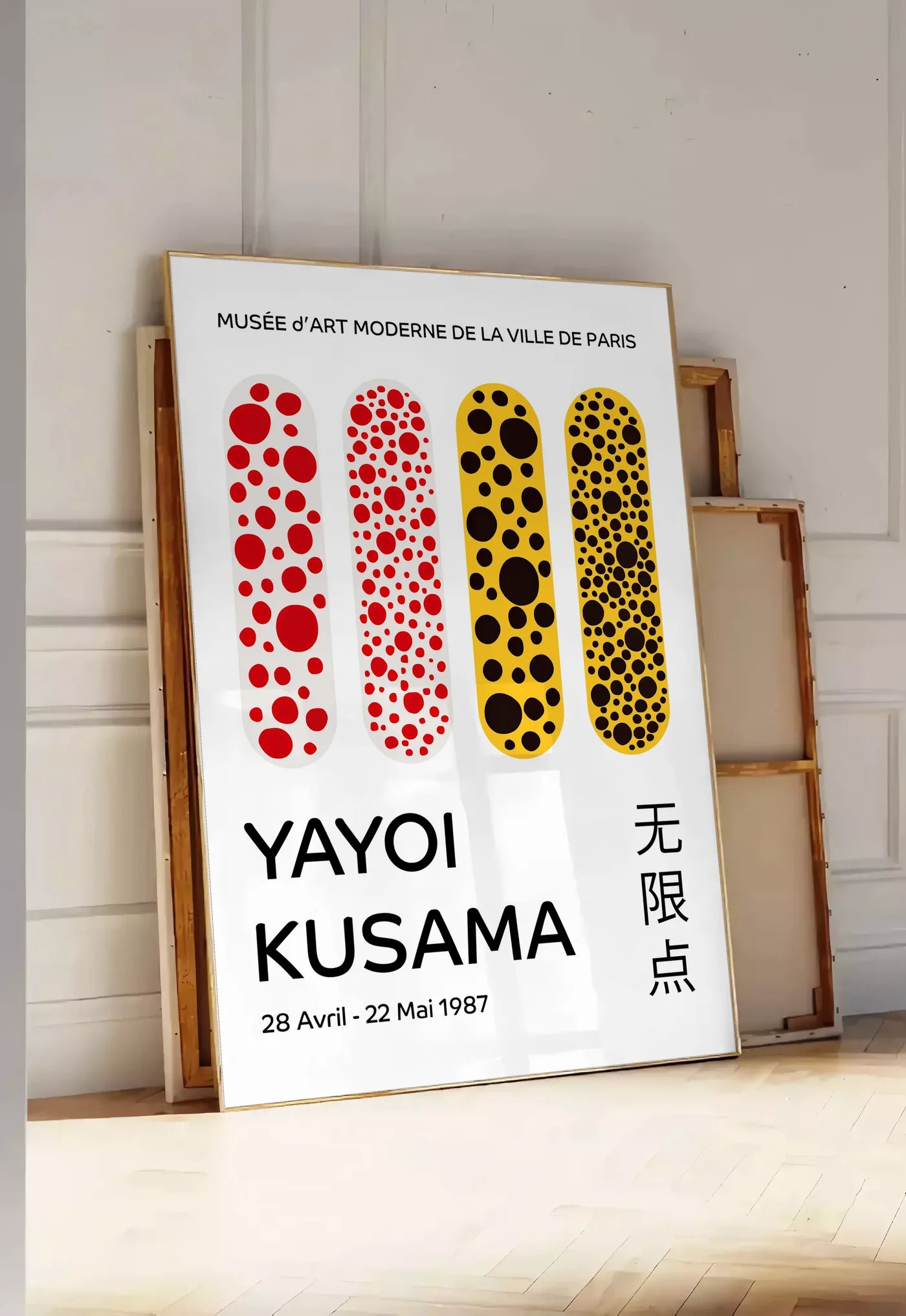 Tirage encadrable affiche capsules a pois de Kusama art japonais, posee au sol dans une entree lumineuse, contre un mur a panneaux blancs, a cote de chassis en bois empiles
