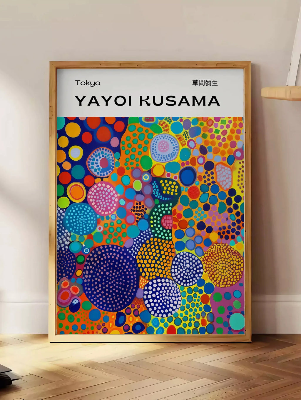 Estampe affiche cercles multicolores de Kusama art japonais, posee au sol dans un coin salon, sur un parquet a chevrons, pres d'une table d'appoint en chene chargee de livres