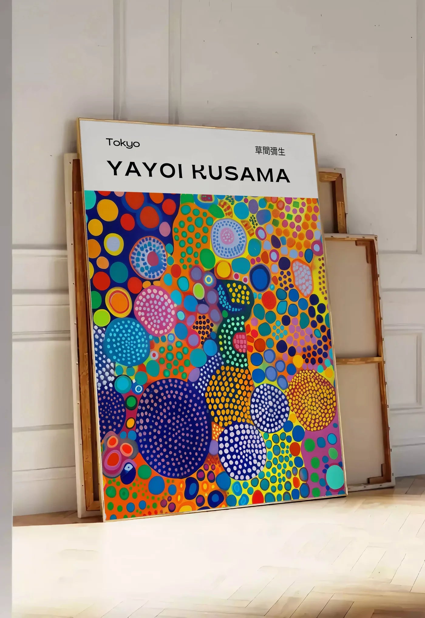 Tirage encadrable affiche cercles multicolores de Kusama art japonais, posee au sol dans une entree lumineuse, contre un mur a panneaux blancs, a cote de chassis en bois empiles