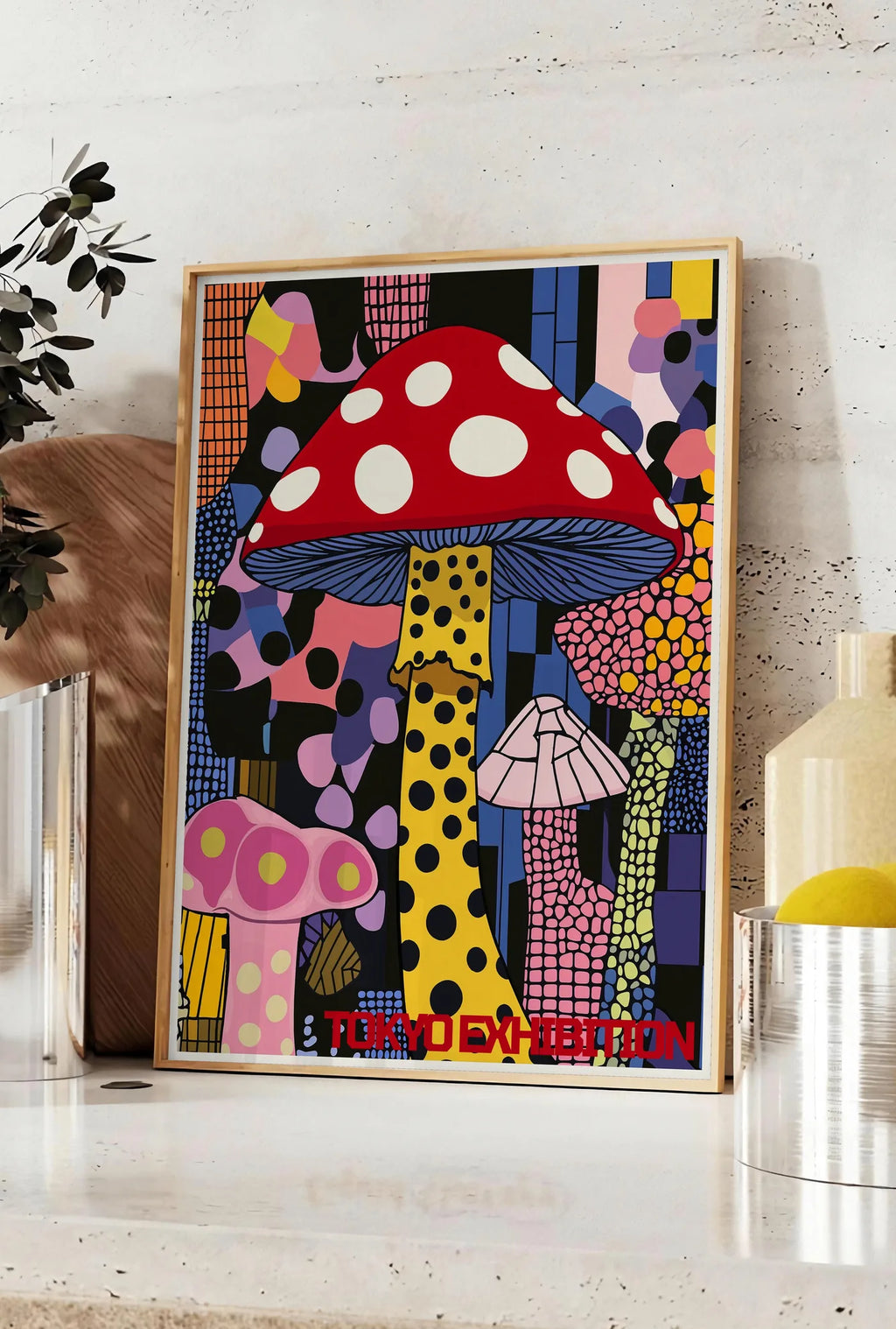 Affiche affiche champignon pop de Kusama art japonais, posee sur un plan de travail de cuisine en pierre claire, entre une branche d'eucalyptus en vase et un bocal de citrons