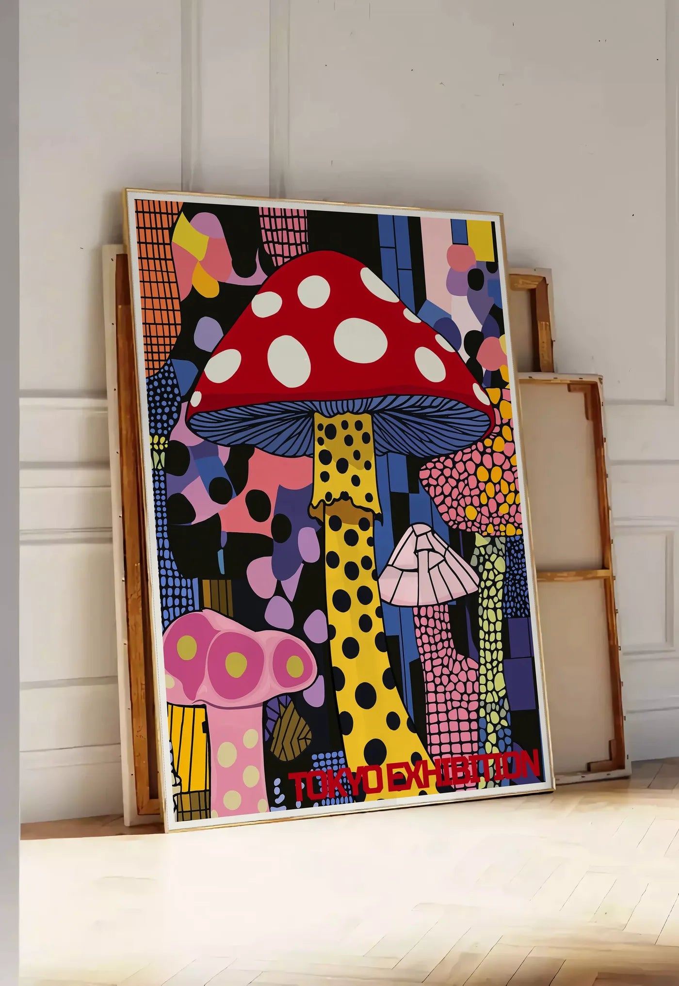 Tirage encadrable affiche champignon pop de Kusama art japonais, posee au sol dans une entree lumineuse, contre un mur a panneaux blancs, a cote de chassis en bois empiles