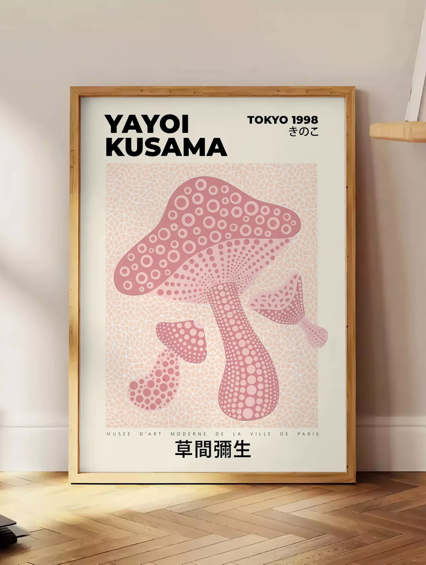Estampe affiche champignon rose de Kusama art japonais, posee au sol dans un coin salon, sur un parquet a chevrons, pres d'une table d'appoint en chene chargee de livres