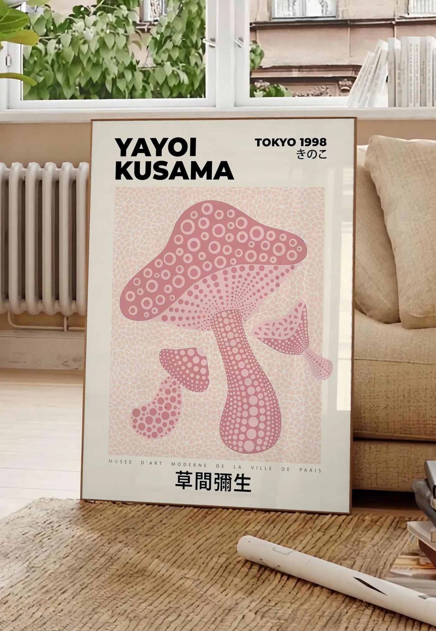 Poster affiche champignon rose de Kusama art japonais, posee au sol dans un salon parisien, devant une grande fenetre donnant sur un immeuble haussmannien, entre un ficus et un canape creme