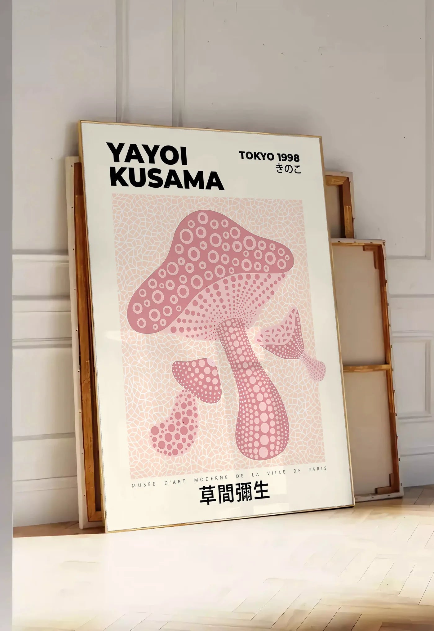 Tirage encadrable affiche champignon rose de Kusama art japonais, posee au sol dans une entree lumineuse, contre un mur a panneaux blancs, a cote de chassis en bois empiles
