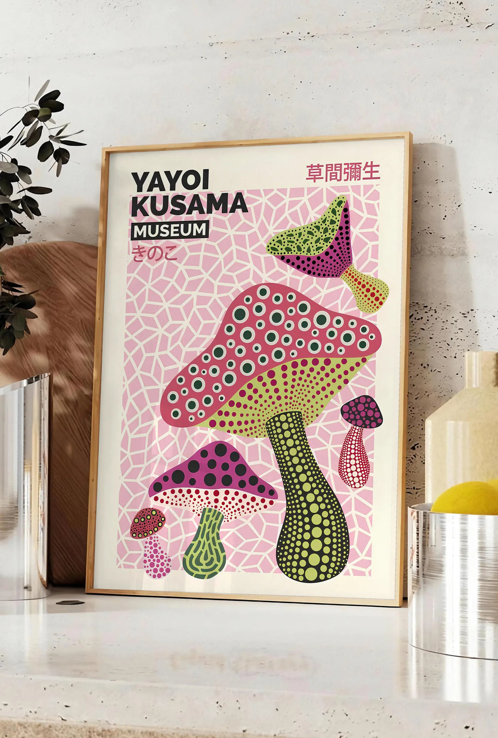 Affiche affiche champignons magenta de Kusama art japonais, posee sur un plan de travail de cuisine en pierre claire, entre une branche d'eucalyptus en vase et un bocal de citrons