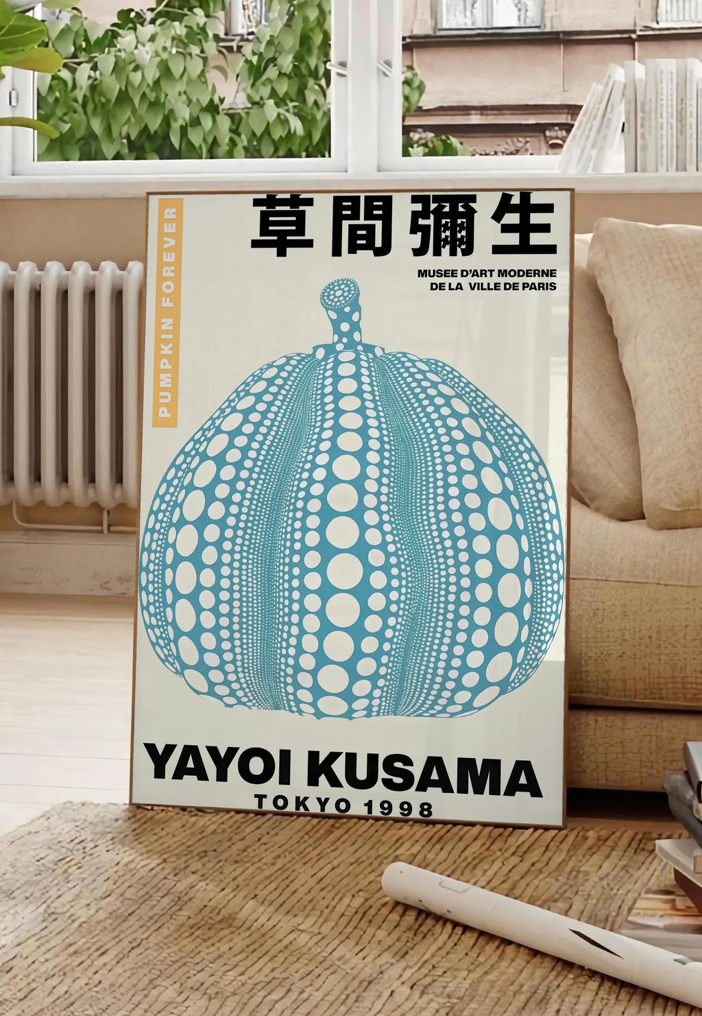Poster affiche Kusama citrouille bleue a pois sur fond creme, posee au sol dans un salon parisien, devant une grande fenetre donnant sur un immeuble haussmannien, entre un ficus et un canape creme