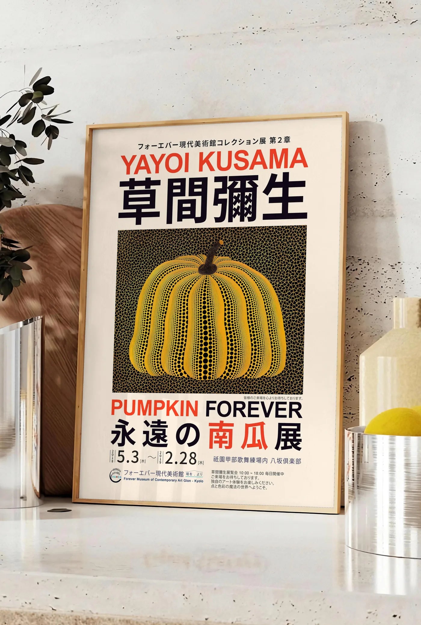 Affiche affiche Kusama citrouille jaune a pois sur fond noir en affiche d exposition, posee sur un plan de travail de cuisine en pierre claire, entre une branche d'eucalyptus en vase et un bocal de citrons