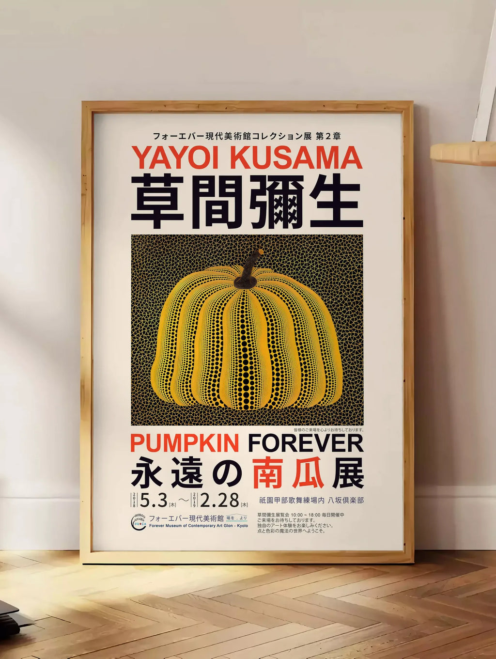 Estampe affiche Kusama citrouille jaune a pois sur fond noir en affiche d exposition, posee au sol dans un coin salon, sur un parquet a chevrons, pres d'une table d'appoint en chene chargee de livres