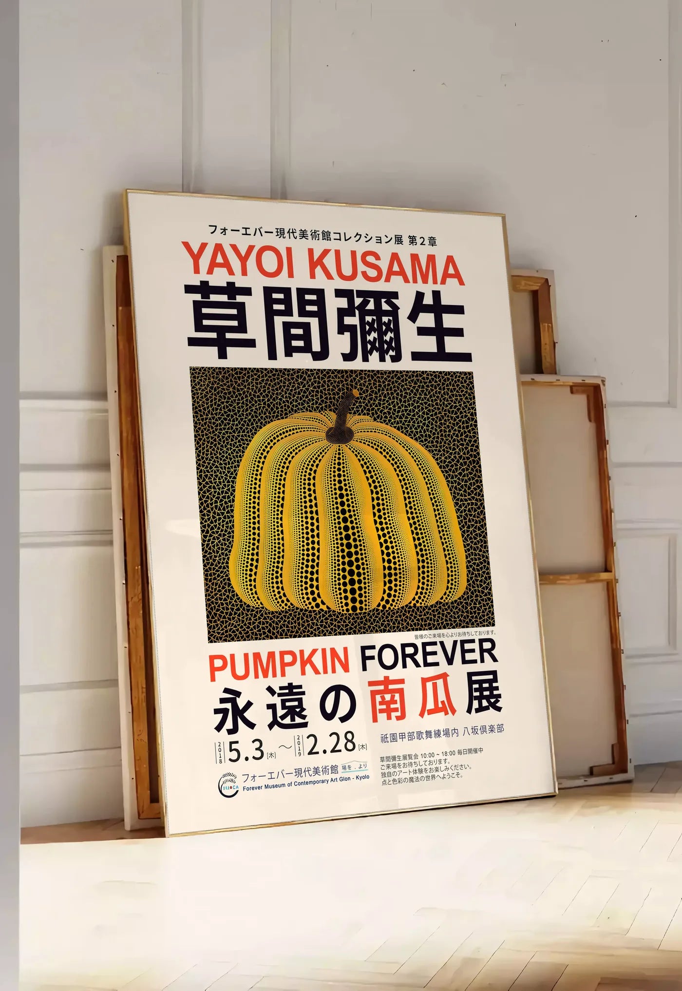 Tirage encadrable affiche Kusama citrouille jaune a pois sur fond noir en affiche d exposition, posee au sol dans une entree lumineuse, contre un mur a panneaux blancs, a cote de chassis en bois empiles