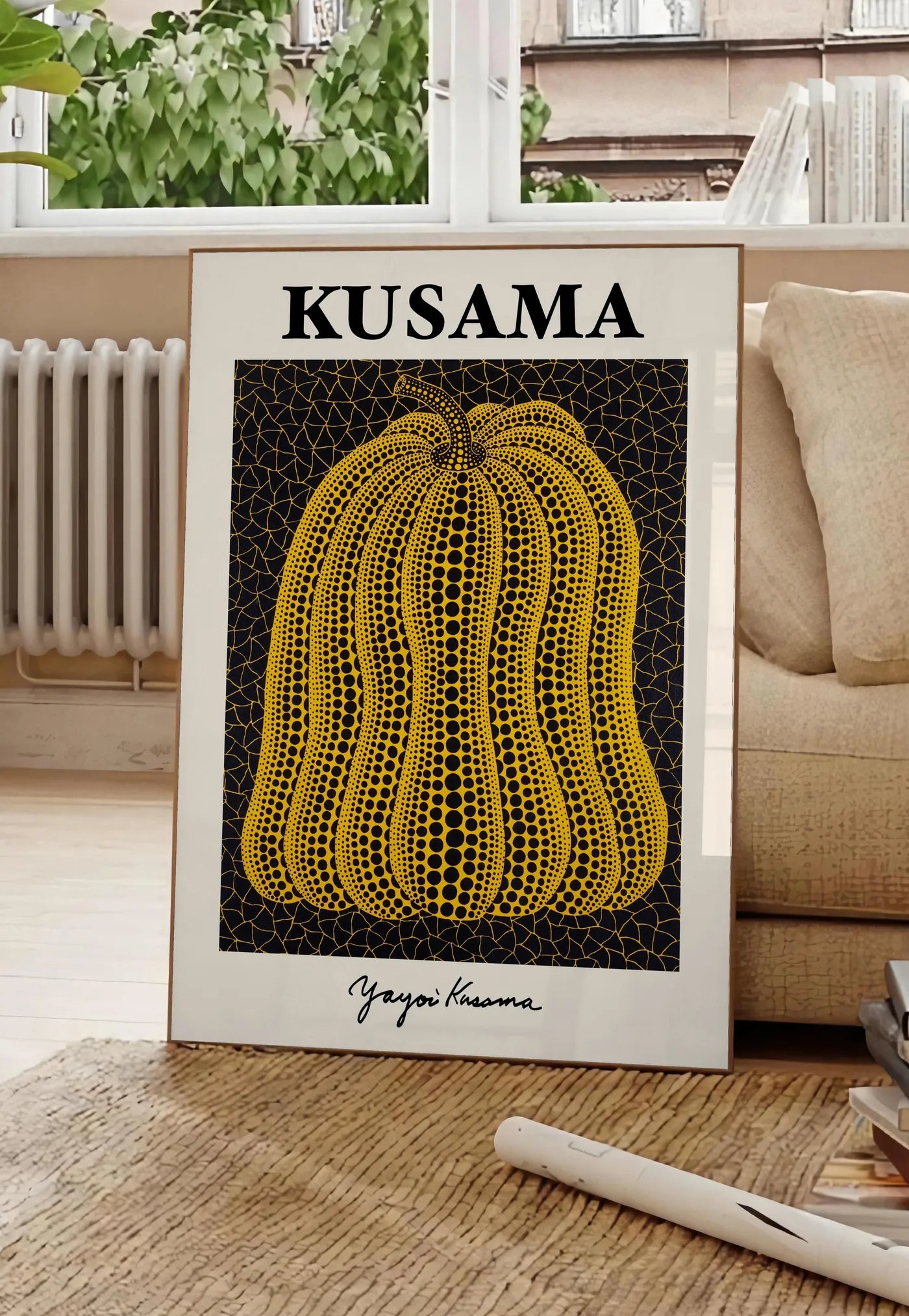Poster affiche Kusama citrouille jaune a pois sur fond noir signe, posee au sol dans un salon parisien, devant une grande fenetre donnant sur un immeuble haussmannien, entre un ficus et un canape creme