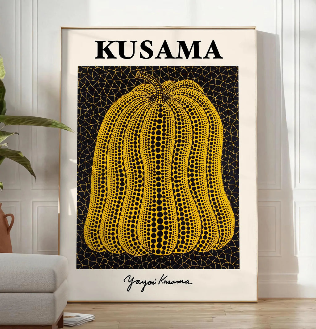 Reproduction affiche Kusama citrouille jaune a pois sur fond noir signe, posee au sol dans un salon minimaliste clair, a cote d'un canape beige et d'une plante verte, sur un parquet clair