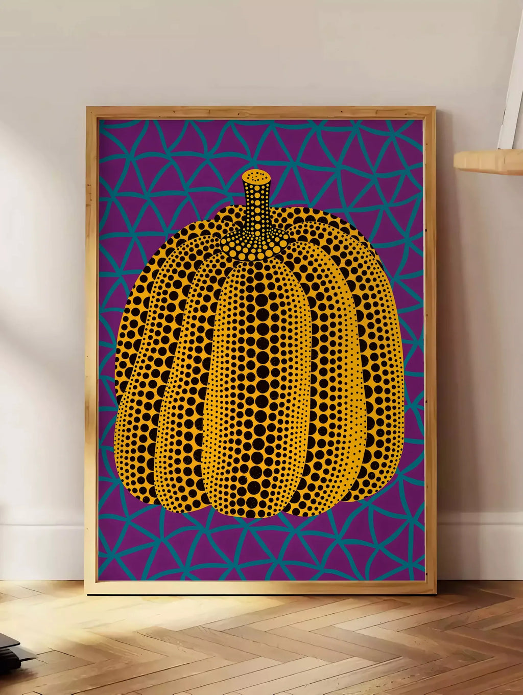 Estampe affiche Kusama citrouille jaune a pois sur fond violet a filet bleu, posee au sol dans un coin salon, sur un parquet a chevrons, pres d'une table d'appoint en chene chargee de livres