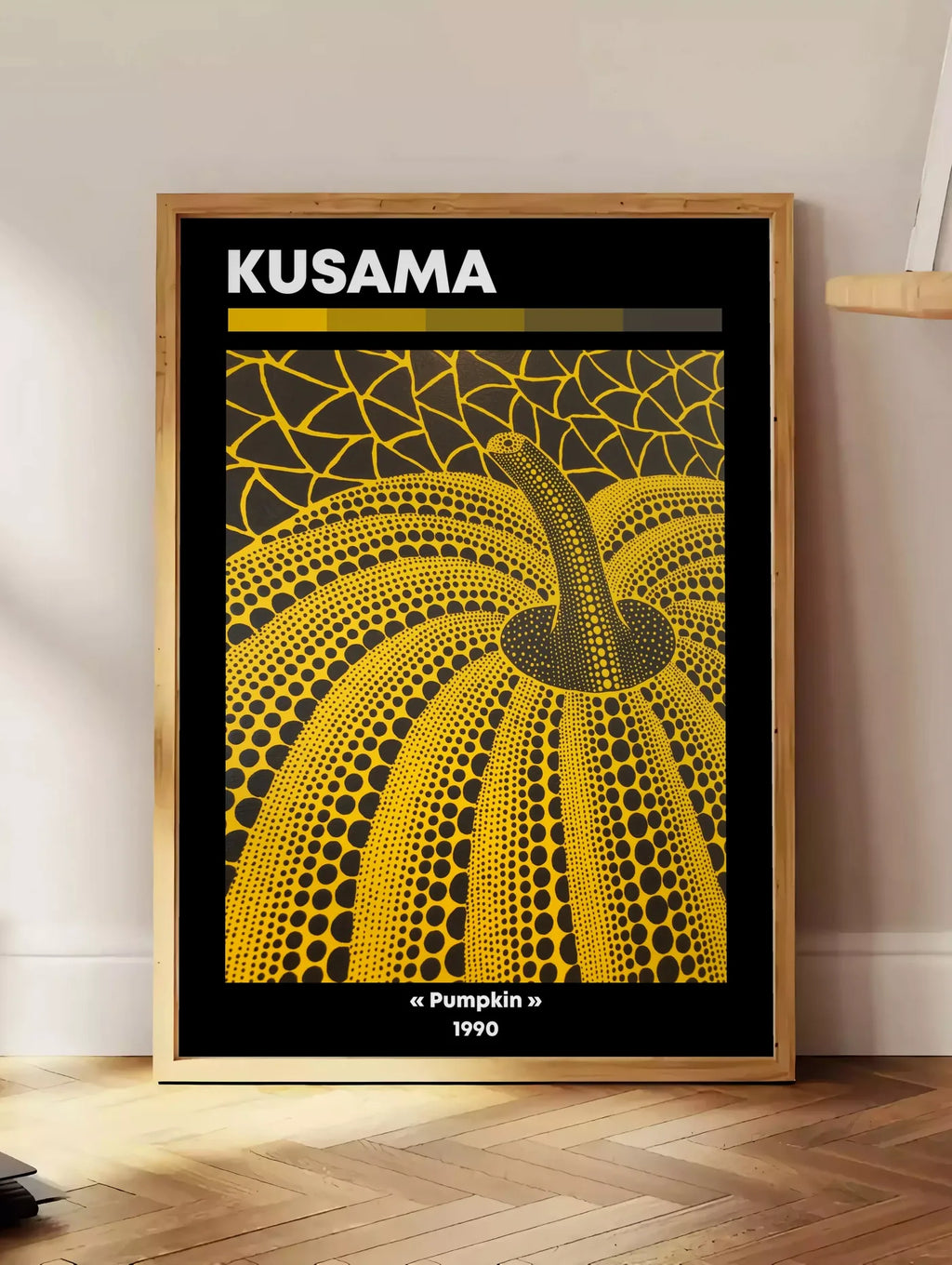 Estampe affiche Kusama citrouille jaune a pois vue en contre-plongee sur fond noir, posee au sol dans un coin salon, sur un parquet a chevrons, pres d'une table d'appoint en chene chargee de livres