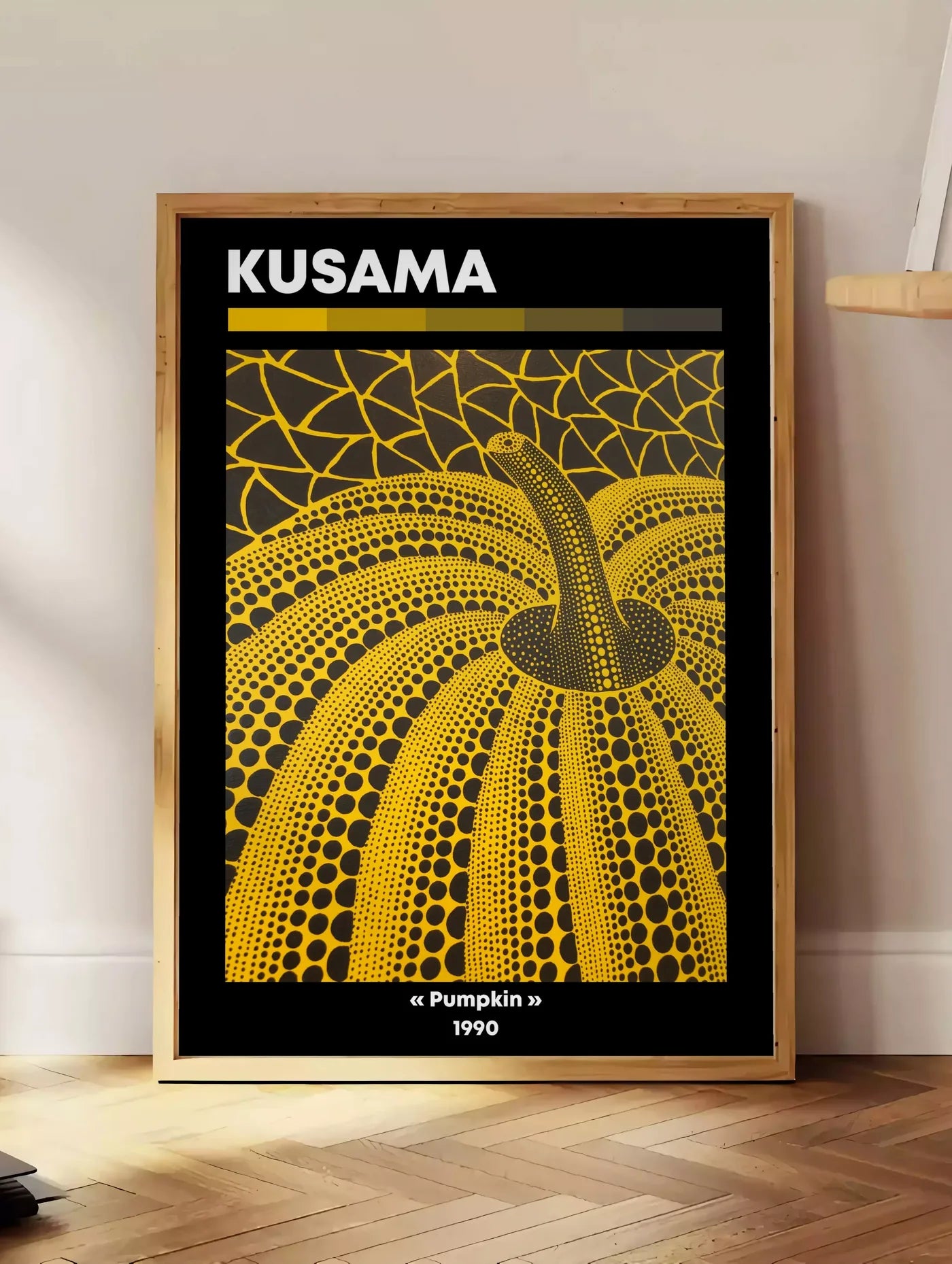 Estampe affiche Kusama citrouille jaune a pois vue en contre-plongee sur fond noir, posee au sol dans un coin salon, sur un parquet a chevrons, pres d'une table d'appoint en chene chargee de livres