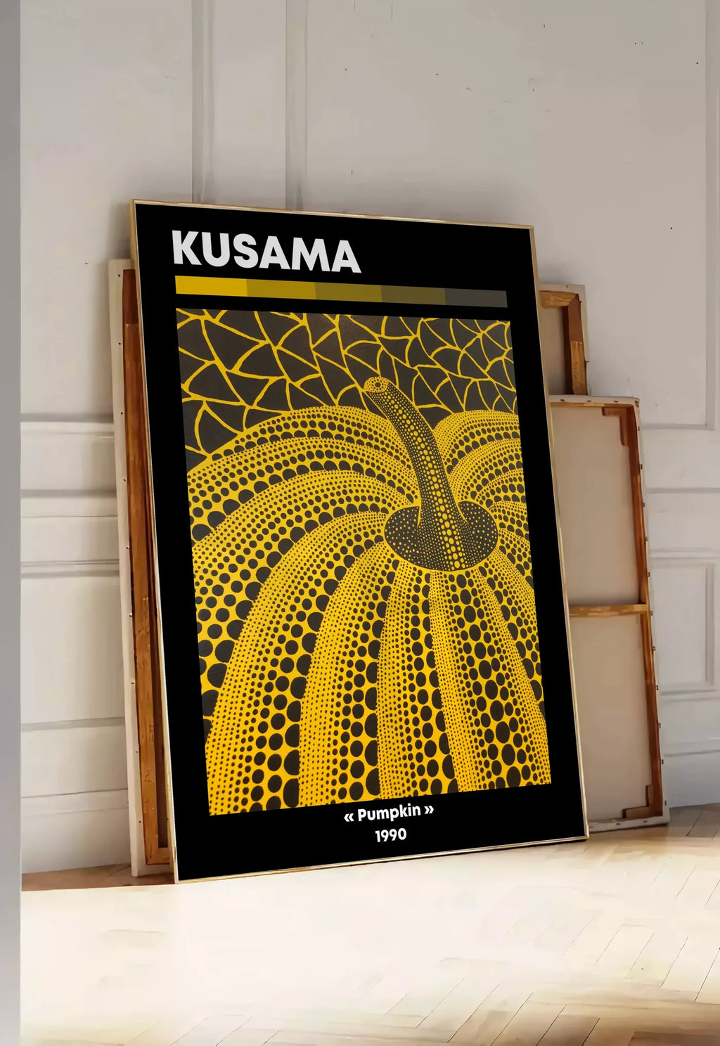 Tirage encadrable affiche Kusama citrouille jaune a pois vue en contre-plongee sur fond noir, posee au sol dans une entree lumineuse, contre un mur a panneaux blancs, a cote de chassis en bois empiles