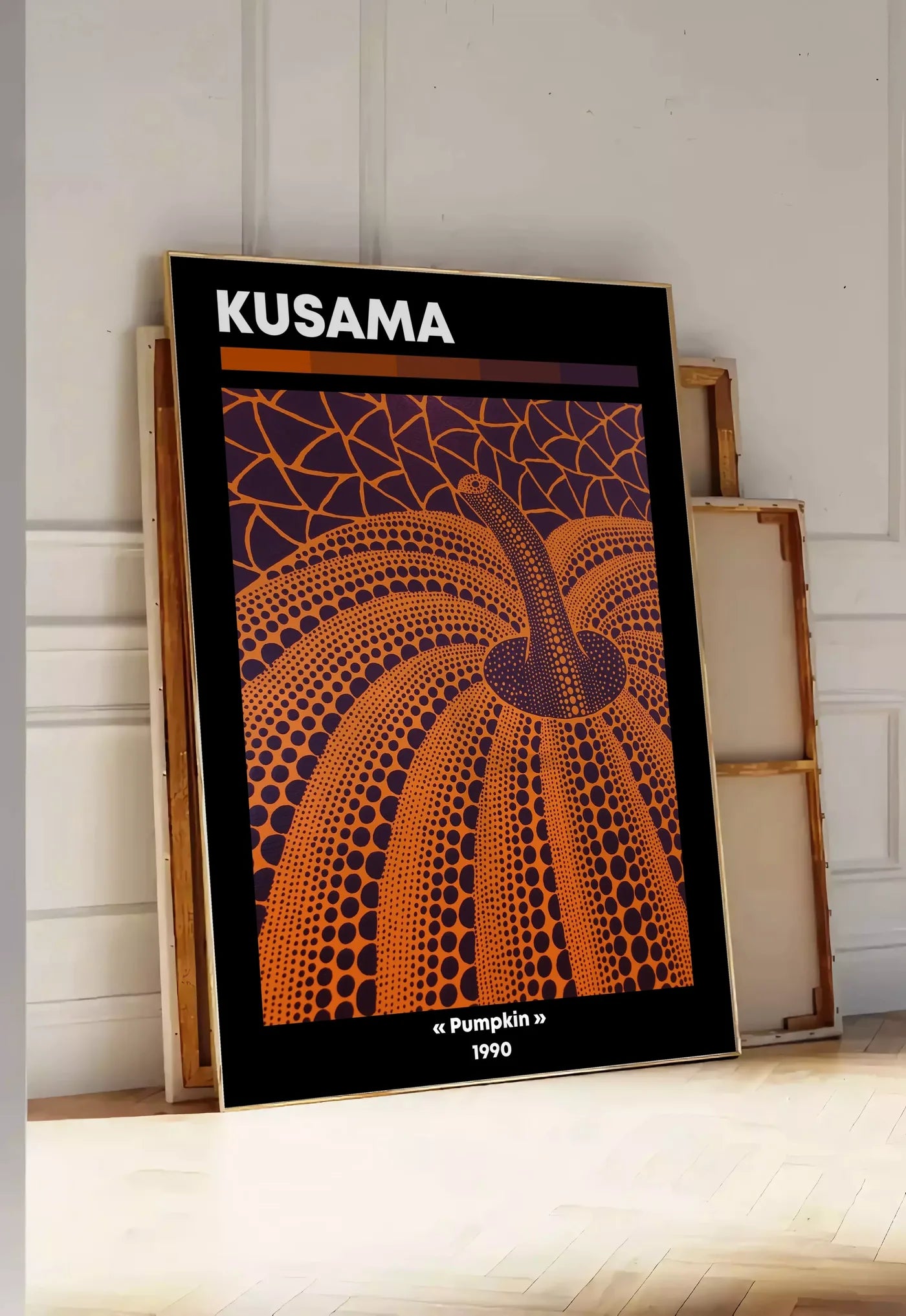Tirage encadrable affiche Kusama citrouille orange a pois vue en contre-plongee sur fond violet, posee au sol dans une entree lumineuse, contre un mur a panneaux blancs, a cote de chassis en bois empiles