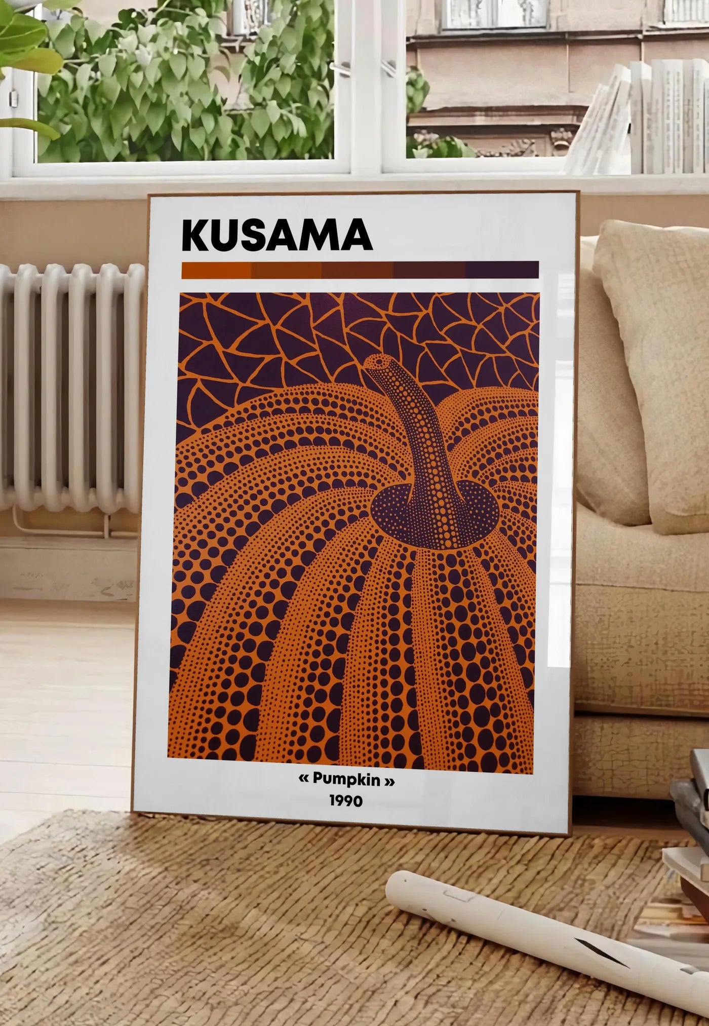 Poster affiche Kusama citrouille orange feu a pois sur fond aubergine, posee au sol dans un salon parisien, devant une grande fenetre donnant sur un immeuble haussmannien, entre un ficus et un canape creme