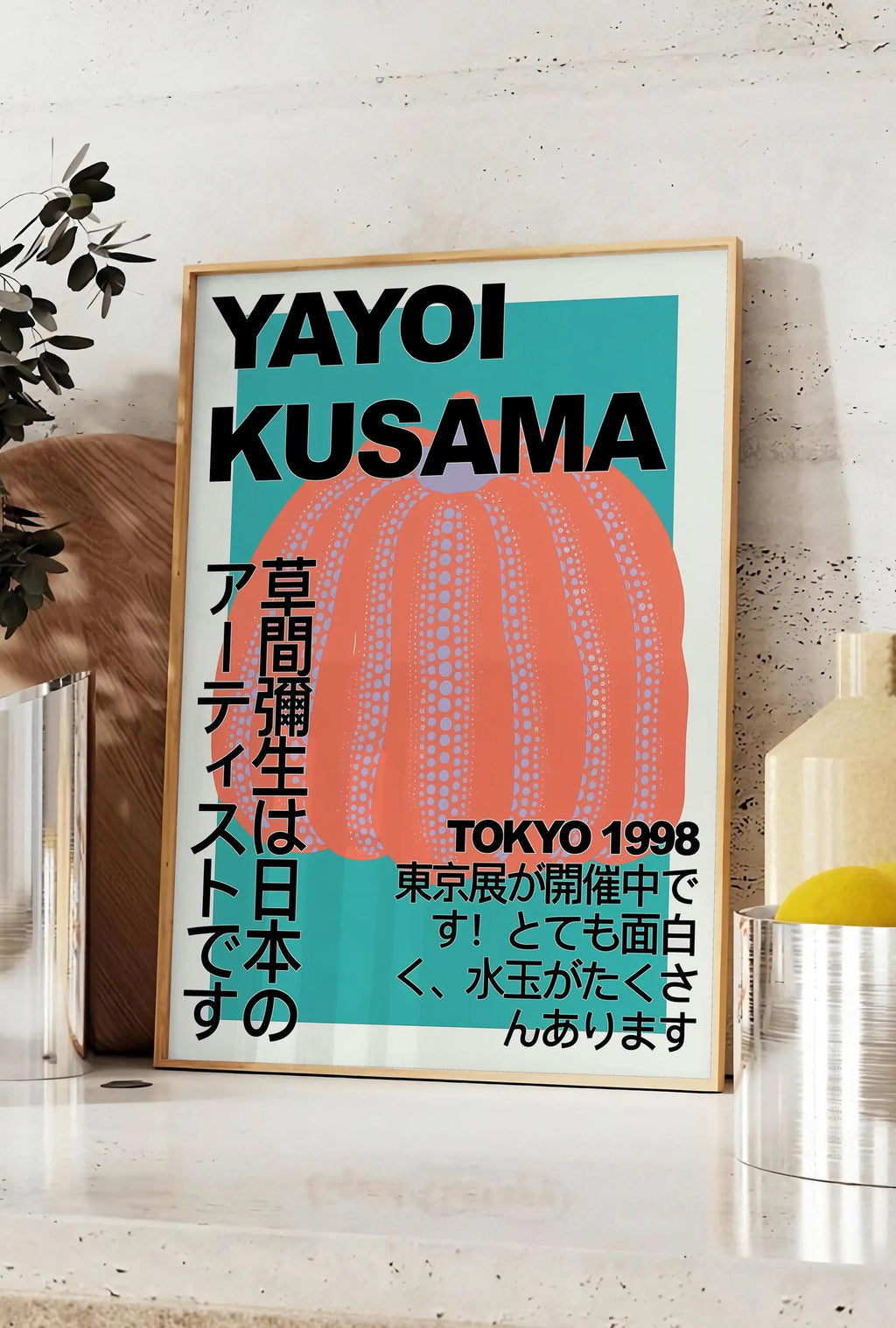 Affiche affiche citrouille orange de Kusama art japonais, posee sur un plan de travail de cuisine en pierre claire, entre une branche d'eucalyptus en vase et un bocal de citrons