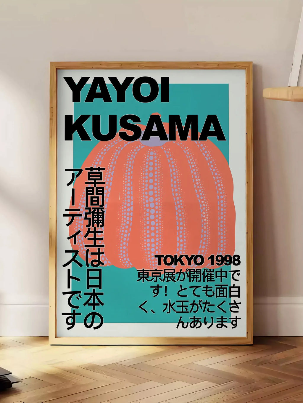 Estampe affiche citrouille orange de Kusama art japonais, posee au sol dans un coin salon, sur un parquet a chevrons, pres d'une table d'appoint en chene chargee de livres